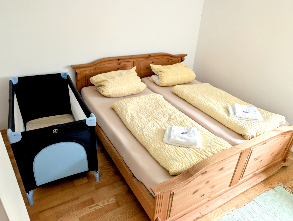 Ruhiges Schlafzimmer mit Doppelbett aus Holz und aufgestelltem Reisebettchen